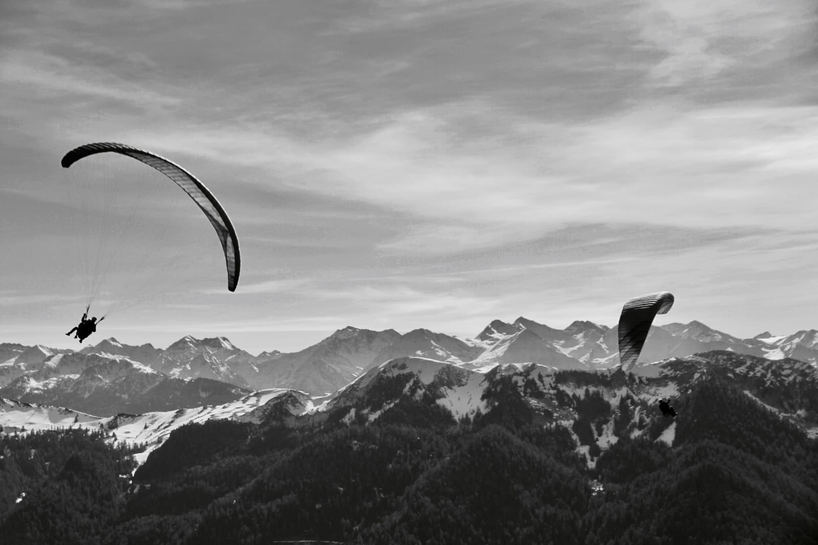 Vol hivernal à deux au-dessus des sommets enneigés, photo en noir et blanc.